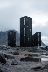 Fototapeta premium Three tall black buildings stand on a rocky landscape with mountains and clouds in the background during a cloudy day in a remote location