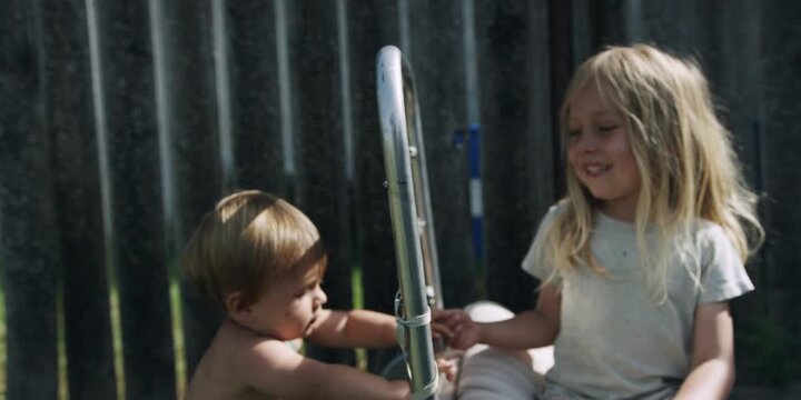 Two children sitting on a sun lounger in a field by a fence