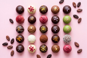 Colorful chocolate truffles and cocoa beans on pastel pink surface