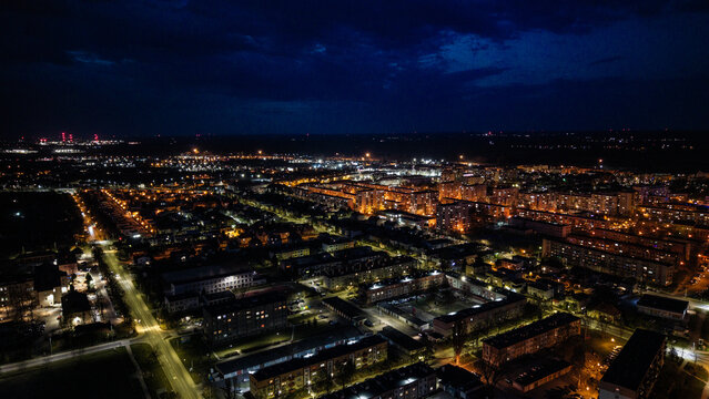 Aerial drone footage of a small provincial town in Poland at night, glowing street lights, quiet urban landscape, peaceful atmosphere, and illuminated roads under dark sky.