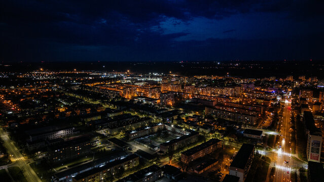 Aerial drone footage of a small provincial town in Poland at night, glowing street lights, quiet urban landscape, peaceful atmosphere, and illuminated roads under dark sky.