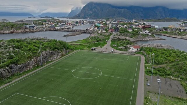 Drone view approaching Henningsv&aelig;r Football Stadium in Lofoten Islands, Norway. Norwegian coastal village and mountains rise behind the famous seaside football field.