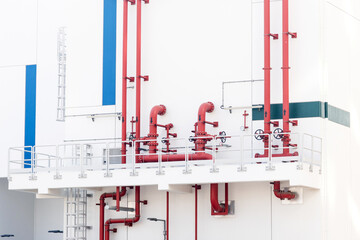 Red pipes and valves delivering essential services on the white exterior of an industrial building with architectural details