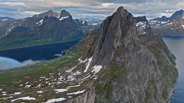 Drone aerial flying past the sharp summit of Segla mountain on Senja Island, Norway. Iconic Norwegian peak towers above fjord waters and rugged Arctic landscape.