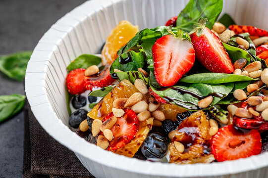 Fresh fruit and nut salad with greens. A bowl holds a mix of fresh strawberries, oranges, spinach, and nuts. This salad is colorful and ready to eat.