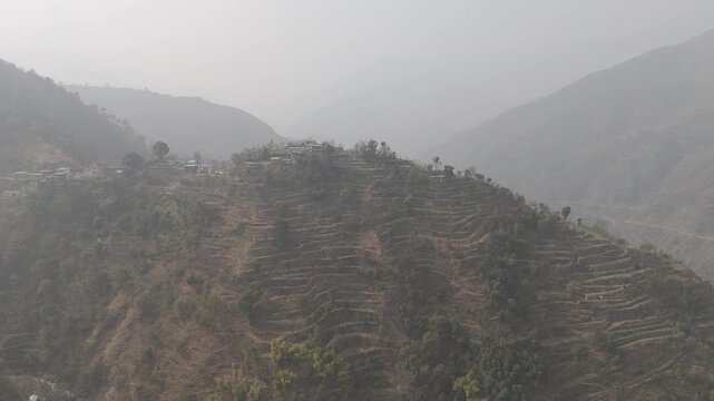 Aerial landscape view of Sainji corn village near Mussoorie, Uttarakhand, with terrace farms and forests of deodar and pine trees on misty slopes in a high-altitude Himalayan region during winter.