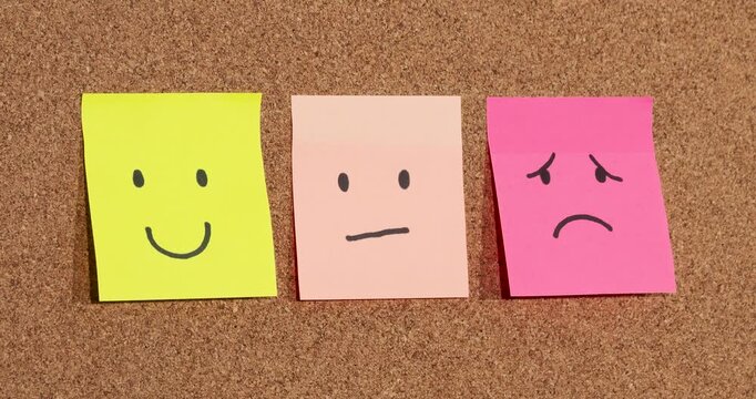 Zoom in to a three sticky notes with human emotion faces representations over a cork background