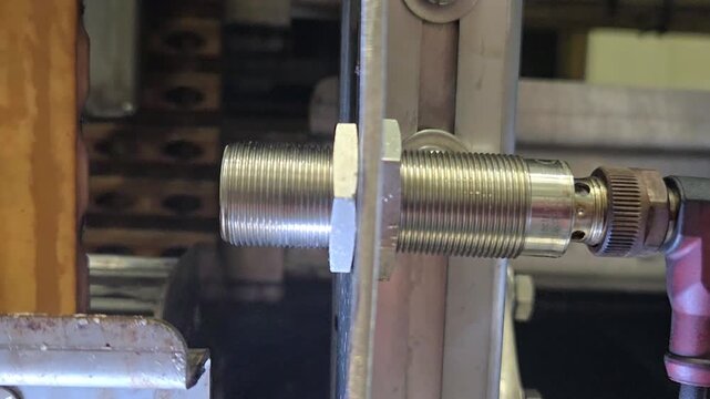 Close-up of an inductive proximity sensor detecting a metal part on an industrial production line.