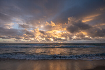 Fototapeta premium Dramatic ocean waves at sunrise with glowing clouds and shoreline reflections
