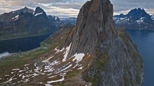 Aerial view circling the dramatic Segla peak above the fjord on Senja Island, Norway. Rugged Arctic landscape with rocky slopes and distant mountain ranges.