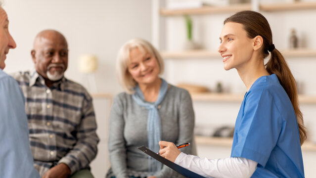 A healthcare professional is talking to three patients in a consultation room. The patients look focused and engaged. The setting appears bright and welcoming.