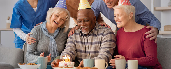 Naklejka premium A group of five people celebrates a birthday in a cozy living room. They smile and gather around a cake with candles on it. They enjoy snacks and drinks while wearing party hats.