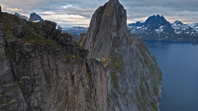 Drone aerial flying past the steep rock wall of Segla mountain on Senja Island, Norway. Iconic Arctic summit towers above fjord waters and alpine scenery.