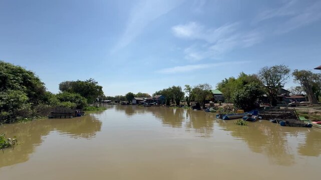 Muddy Sangker river with stilt houses along the banks between Tonle Sap Lake and Battambang Cambodia. Daily activities of local residents in Southeast Asia.