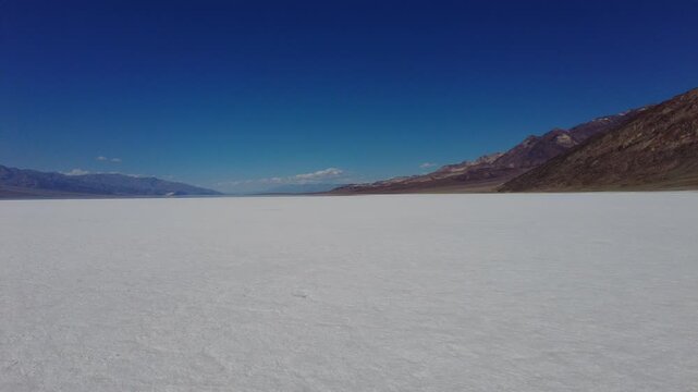 A steady panoramic sweep across the expansive white salt flats of Badwater Basin. Scenic desert landscape featuring the contrast between the white valley floor and the towering brown mountains.