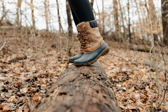 A close up of hiking boots stepping on a log in the wilderness.