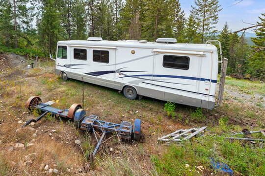 A Class A size motorhome RV recreational vehicle sits in a wooded mountain field alongside two trailers in North Idaho, USA.