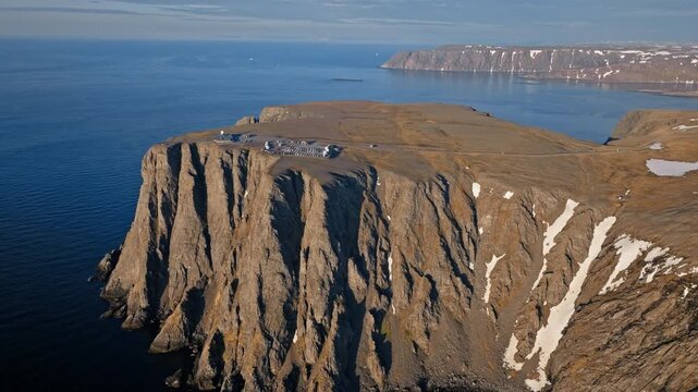 Drone aerial revealing the steep cliffs of North Cape at Nordkapp, Norway. Rugged Arctic coastline stretches along the Barents Sea horizon.