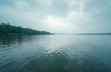 Fototapeta premium Calm lake water reflects cloudy sky and distant tree line on horizon. Serene natural landscape offers peaceful waterscape and quiet mood for outdoor recreation or eco themes.