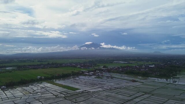 Aerial panoramic view of Kawi and Arjuno mountains peak over lush green rice fields in East Java.
