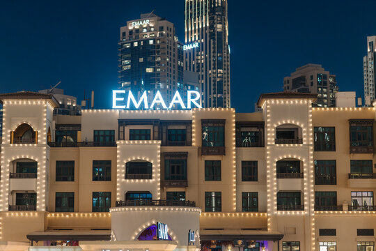 Emaar building illuminated at night with modern skyscrapers in the background, showcasing Dubai's architectural landscape