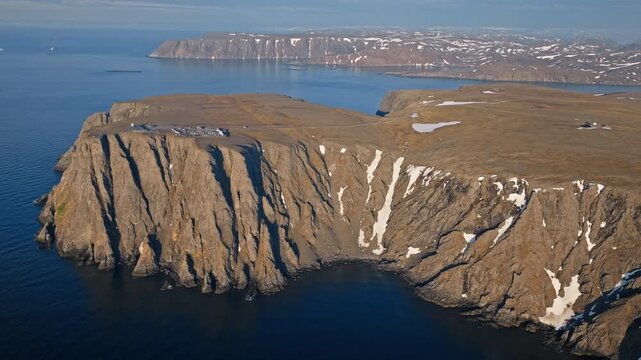 Drone aerial revealing the massive Nordkapp cliffs rising from the Barents Sea. Arctic coastal plateau sits above steep rock formations.