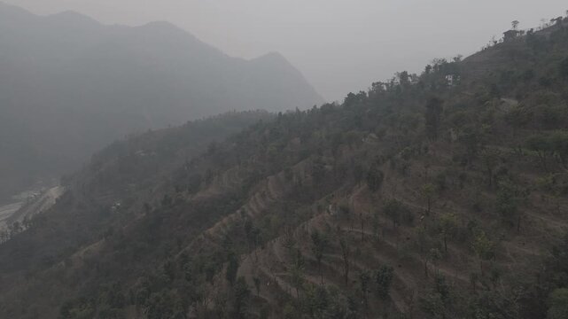 Aerial landscape view of Dwara village near Dehradun, Uttarakhand, showing misty mountains with terrace farming slopes and forests of sal, chir pine, khair, and sissoo on a winter evening.