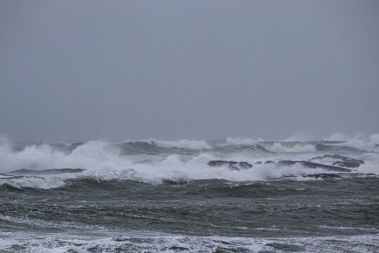 Powerful sea waves crashing against a rocky shoreline under a heavy overcast sky