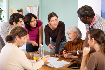 Obraz premium Group of people of different ages are sitting at a table and talking to each other, they are having a discussion and looking at documents. Office employees discuss the launch of the project