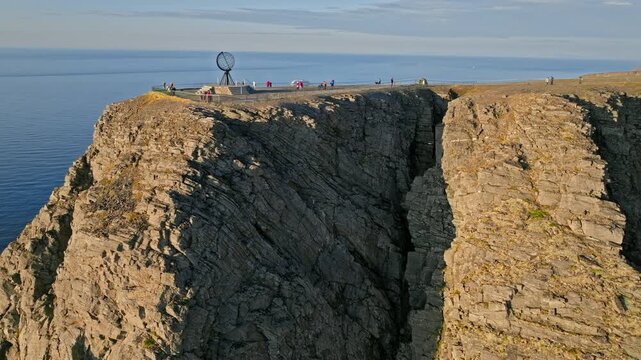 Aerial view of the Nordkapp globe monument perched above steep Arctic cliffs in Norway. Tourists gather at the northernmost viewpoint above the Barents Sea.
