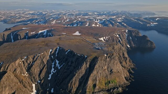 Drone aerial flying along the dramatic Nordkapp cliffs in northern Norway. Rugged Arctic coastline towers above the calm Barents Sea.