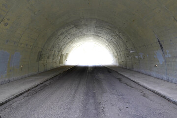Obraz premium Symmetrical view of a bright light at the end of a dark concrete road tunnel portal