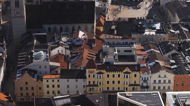 Aerial pan and descent reveal Brixen, South Tyrol, Italy, with red roofs, pastel facades, cathedral clock tower, cobbled lanes, piazza fountain, and late winter snow.