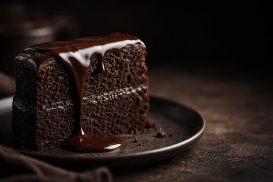 Fatia de bolo de chocolate com calda cremosa escorrendo em prato escuro
