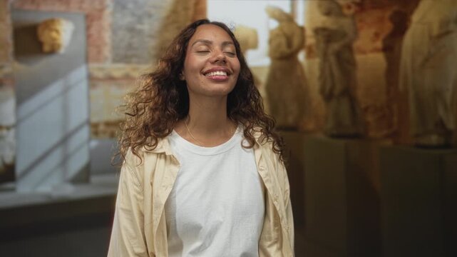 Woman smiling with face visible and eyes closed amid stone statues in the museum building; quiet joy.