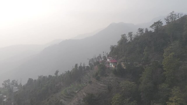 Landscape view from Kuee village in Tehri Garhwal, Uttarakhand, showing misty mountains and forested hills under clouds on a calm winter evening.