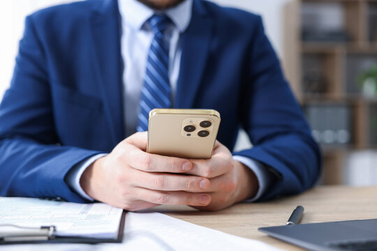 Man using modern smartphone at wooden desk in office, closeup