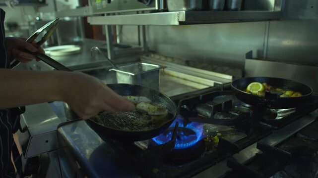 Chef working in restaurant kitchen hot flame stove basting fish with butter