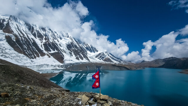 Nepal Flag fluttering in the wind at Lake tilicho, highest lake in the world, with himalayan mountains and glaciers in the background