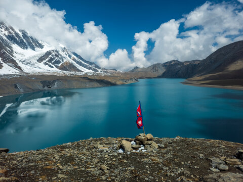 Nepal Flag fluttering in the wind at Lake tilicho, highest lake in the world, with himalayan mountains and glaciers in the background