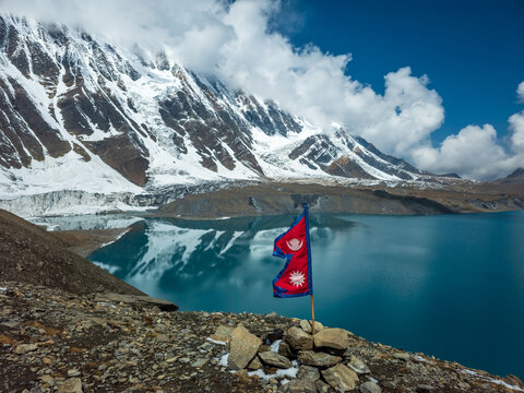 Nepal Flag fluttering in the wind at Lake tilicho, highest lake in the world, with himalayan mountains and glaciers in the background
