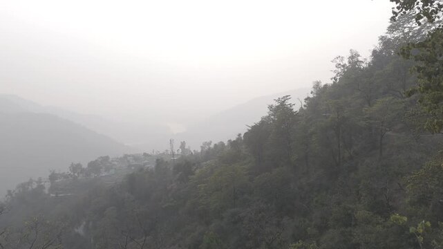 Landscape view from Kuee village in Tehri Garhwal, Uttarakhand, showing misty mountains and forested hills under clouds on a calm winter evening.
