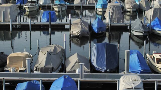 Panning shot over a row of small motorboats and yachts moored at the city harbor on Lake Lucerne on a calm day.