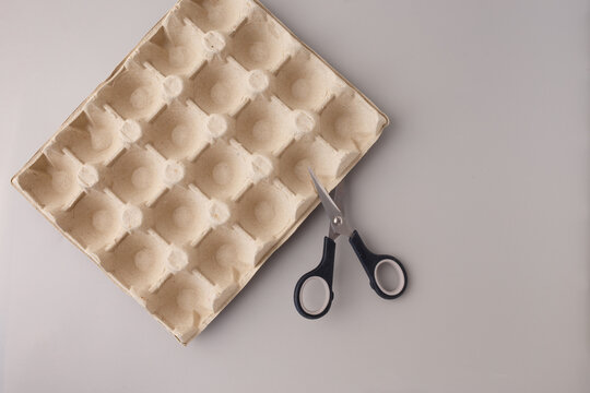 Egg carton tray with scissors on grey background. Recycled material for DIY craft preparation. Eco reuse concept. Design for poster, banner, card. Flat lay composition with copy space,