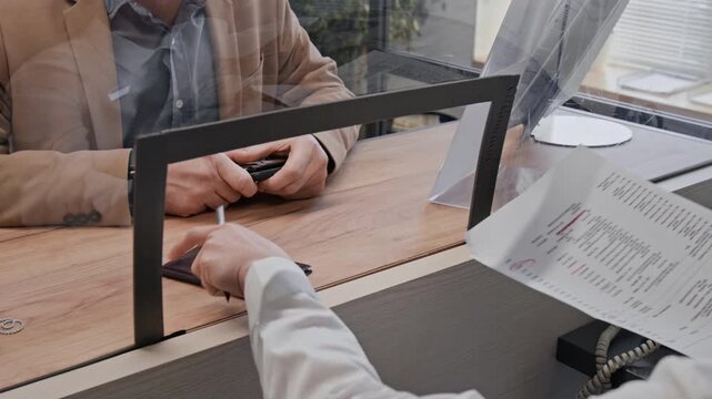 High angle close up shot of young female bank teller handling documents of unrecognizable male customer in bank office