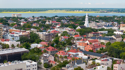 Naklejka premium Aerial view of downtown Charleston, South Carolina skyline showing rooftops, historic churches and buildings, trees, and the waterfront in a sunny morning cityscape landscape