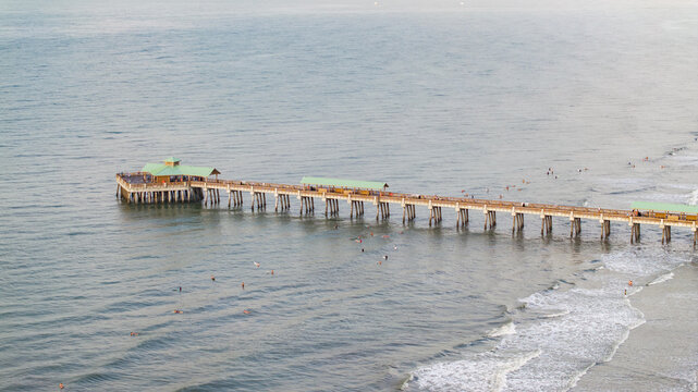Aeral view of Folly Beach pier in Folly Beach town near Charleston, South Carolina showing the coastline with people and surfers enjoying the water and waves during morning light