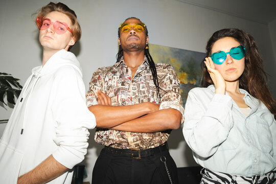 Three young adults pose with colorful heart-shaped sunglasses, showcasing a bold and fashionable style.