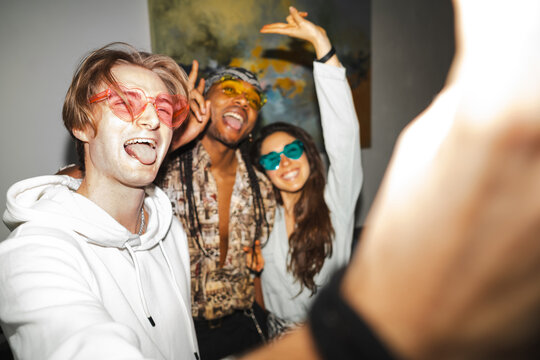 Three young friends wearing colorful sunglasses laugh and pose for a photo at a vibrant party, capturing a moment of joy and connection.