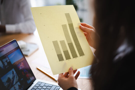 A person reviews a bar chart showing data from April to July, with a laptop open on the table.